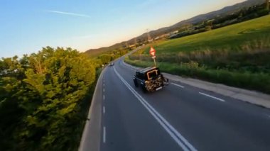 Cinematic FPV shot of Gray Stylish landrover with motorcycle on the back driving on the green field road during beautiful sunset. High quality 4k footage