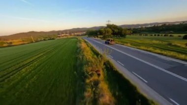 Cinematic FPV shot of Gray Stylish landrover with motorcycle on the back driving on the green field road during beautiful sunset. High quality 4k footage