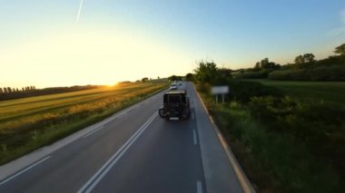Cinematic FPV shot of Gray Stylish landrover with motorcycle on the back driving on the green field road during beautiful sunset. High quality 4k footage