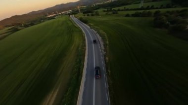 Dynamic aerial shot of Gray Stylish suv with motorcycle on the back driving on the green field road 