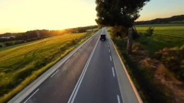 Cinematic FPV shot of Gray Stylish landrover with motorcycle on the back driving on the green field road during beautiful sunset. High quality 4k footage