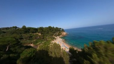 Dynamic fpv drone shot between trees and along the beach full of colourful umbrellas at Mediterranean Sea in Tossa de Mar, Costa Brava In Spain, Catalonia Aerial view. High quality 4k footage