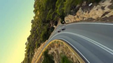 Güneş doğarken Serpentine yolunda hızlı motosiklet sürmek, siyah gömlekli sürücüler. Ardından yüksek hızlı fpv drone, dikey konsept 4k video 50fps