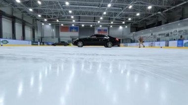 Karargah Fpv İHA 'sı buz hokeyi sahasında siyah arabanın altında kayıyor. Hava Aracı Yüksek Açı İzleme Çekimi. Yüksek kalite 4k görüntü