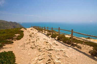 Portekiz 'in suluboya çizimleri, Cabo da Roca Burnu, yürüyüş yolları ve okyanus manzarası, Atlantik okyanusunun üzerindeki uçurum, Atlantika' daki gök mavisi su, uçurumun üzerindeki ahşap tırabzanlar.