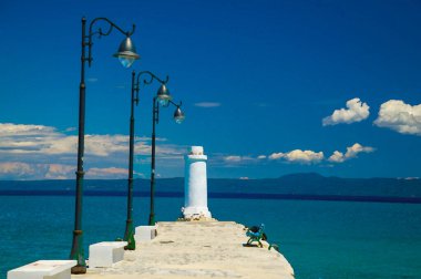 Banklı White Pier Rıhtımı 'nın suluboya çizimi, Toroneos Kolpos Körfezi' nin mavi cennet sularındaki deniz feneri, Pefkohori, Halkidiki, Yunanistan 'da Sithonia yarımadası üzerindeki mavi gökyüzü beyaz bulutları