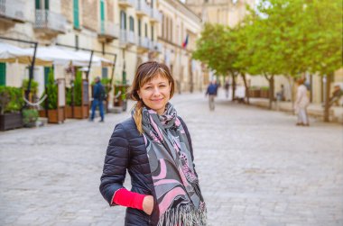 Siyah ceketli genç ve güzel bir kadın gezgin. Kameraya bakıyor, gülümsüyor ve Matera şehrinin tarihi merkezinde poz veriyor. Eski binaların arka planında, İtalya 'da tatilde olan bir kız.