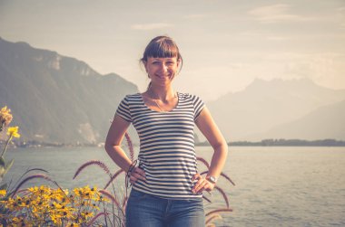 Çizgili gömlekli, kot pantolonlu genç bir kız İsviçre Rivierası 'nın Montreux şehrinde Leman Cenevre Gölü' nün setinde poz veriyor ve gülümsüyor.