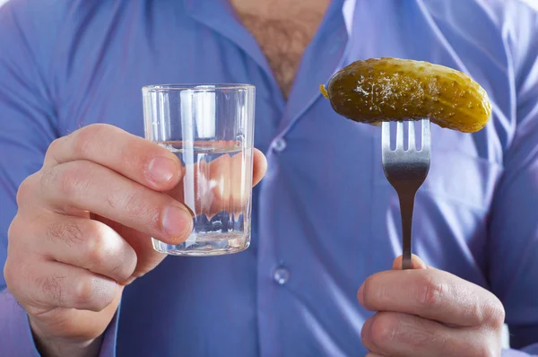 Man met een glas wodka en een komkommer op een vork in zijn hand Rechtenvrije Stockfoto's