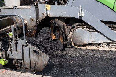 Asfaltlama makinesinin asfaltlaması tamir altındaki bir caddeye asfalt yayıyor.