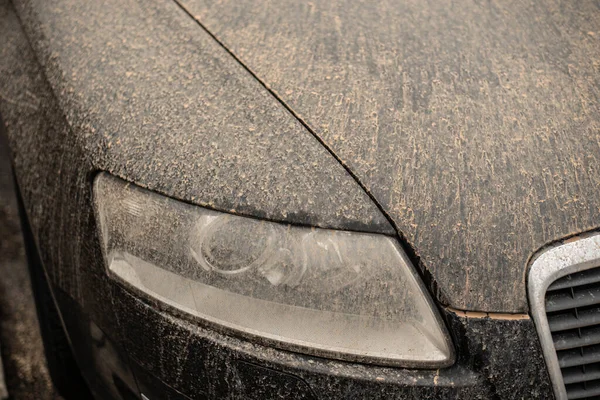 the front light and varnish of a black car in Germany after rain polluted with sahara sand