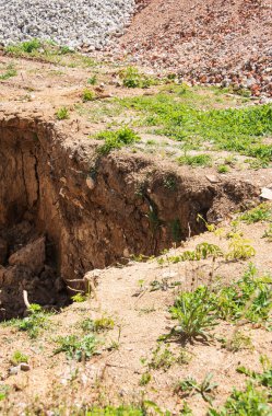 Arka planda yıkılmış bir binanın enkaz yığını olan bir inşaat alanında bir çukur kazmak.
