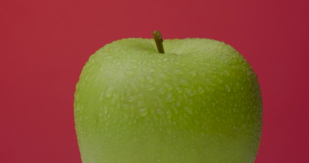 Verde manzana mojada gira colgando sobre un fondo rojo, aislado. — Vídeos de Stock