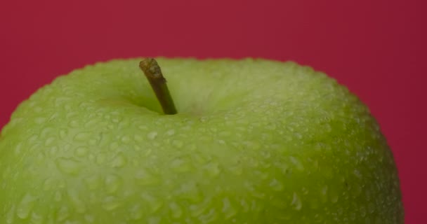 緑のぬれたリンゴは赤い背景にぶら下がって回転し、隔離されます. — ストック動画