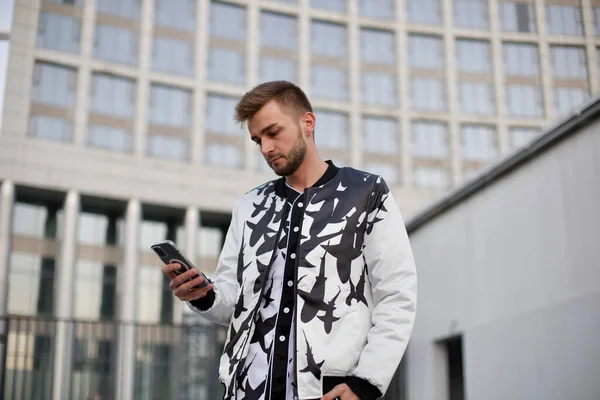 Beyaz ve siyah takım elbiseli yakışıklı adam telefona bakıyor. Kirli sakallı ve modaya uygun takım elbiseli bir adam fotoğraf çekimi sırasında önemli sorunları çözer..