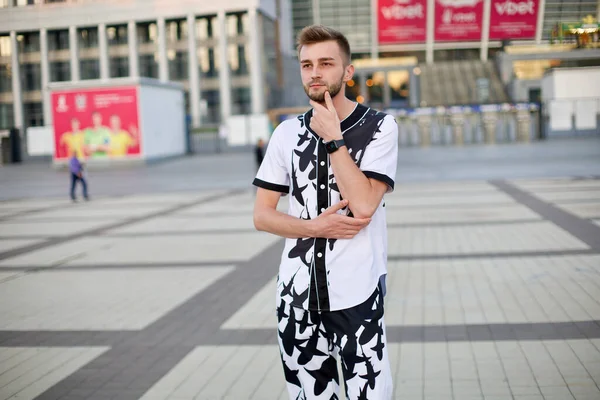 A handsome man in a white and black suit with a hand near his chin. A guy with stubble and a model hairstyle in a trendy suit thought while taking a photo.