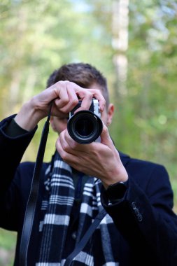 Photographer in a black coat and scarf with a camera at work. Guy takes pictures on the camera. The photographer guy in a coat and scarf shoots at the camera.