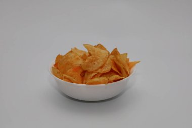 Beyaz arka planda bir tabak çip. Beyaz arka planda baharatlı lezzetli cipslerle dolu beyaz tabak..