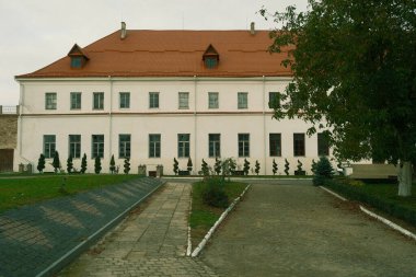 Parkta kırmızı kiremitli çatısı olan güzel beyaz ve sarı bir bina. Şehirdeki parktaki tuğla sarısı bina. Kırmızı kiremitli güzel bir bina.