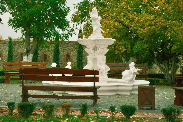 Beyaz fıskiyeli güzel bir park. Parktaki bankların etrafında doğaçlama ağaçlardan oluşan bir çit. Beyaz fıskiyeli ve heykelli parkta güzel bir organizasyon ve manzara