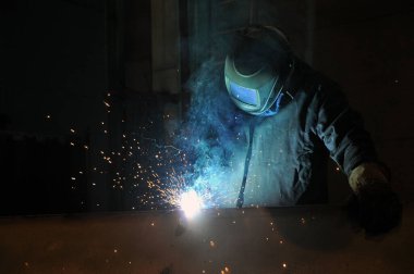 Elektrikli kaynakçı. Bir işçi bir fabrikada metal yapılar kaynak yapar. Meslekler.