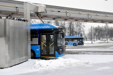 Moskova, Rusya - 30 Ocak 2022: Şarj olurken şarj istasyonunda elektrikli otobüs. Sert kış koşullarında çalış. Kötü çekim koşulları. Kar yağıyor..