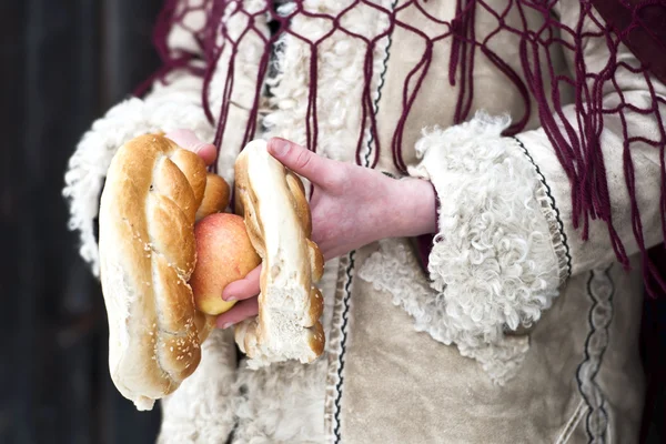 Закрыть руки, держащие яблоко и крендель ребенка, одетого в традиционную румынскую одежду Стоковое Фото