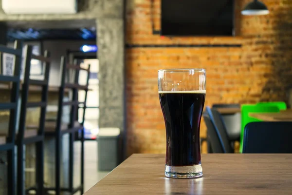 在漂亮的酒吧的木制柜台上喝着一杯深色啤酒.酒吧背景上的深色啤酒.... 图库图片