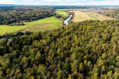 Arka planda yoğun orman, tarım alanları ve nehir üzerinde insansız hava aracı uçuşu