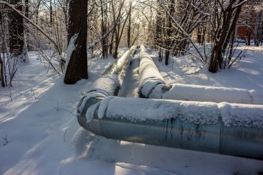 Yerin üstünde sıcak suyu olan büyük borular, kışın karla kaplı borular.