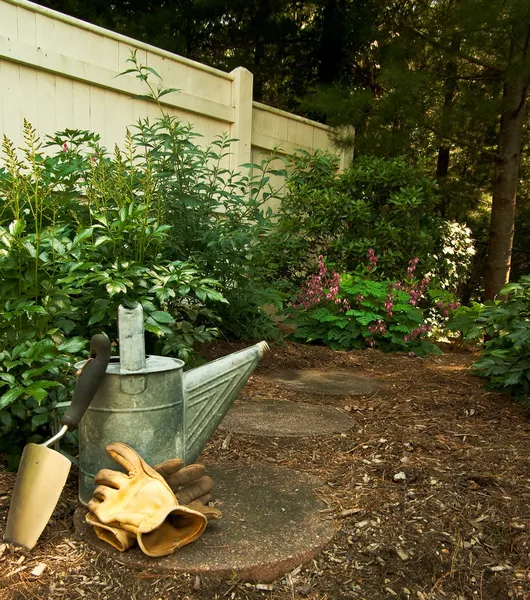 A Trowel, Garden Gloves and Old Watering Can Sit on a Stone Path Stock Photo