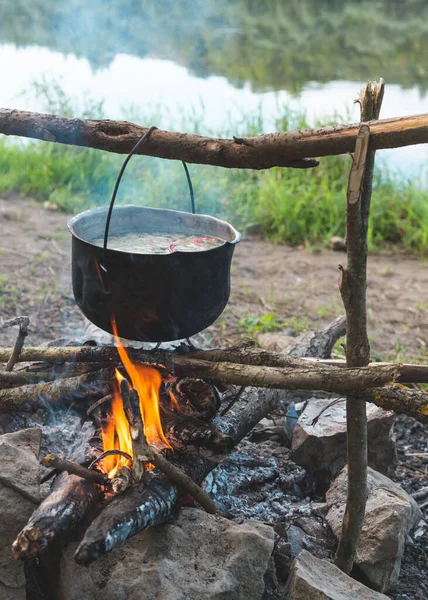 Vaření rybí polévku v hrnci na ohni na břehu řeky — Stock fotografie
