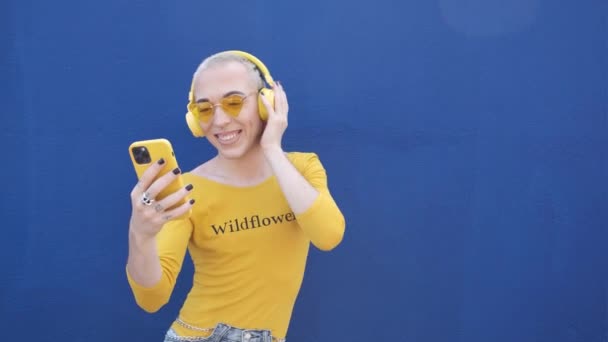 Молодой гей с помощью смартфона и наушников - желтый и синий - lgtbiq концепции — стоковое видео
