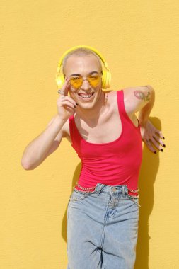 Açık havada kablosuz sarı kulaklıklarla müzik dinleyen güler yüzlü bir genç..