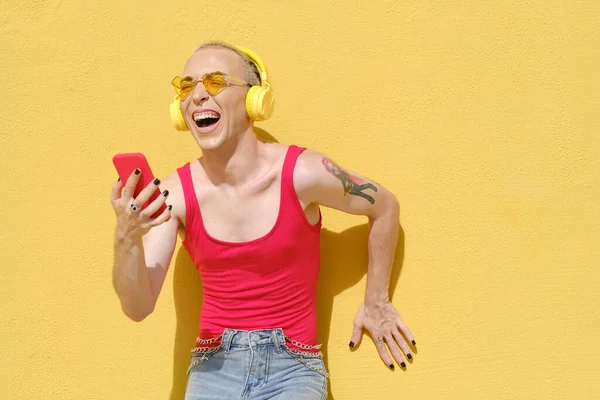 Joven persona no binaria riendo y divirtiéndose mientras disfruta escuchando música con auriculares y un teléfono móvil. —  Fotos de Stock