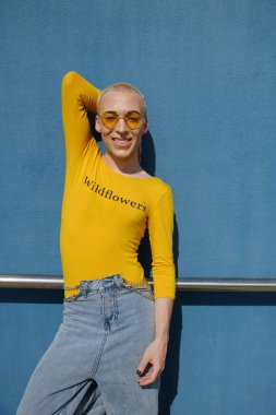 Kendine güveni olmayan genç biri kameraya bakıyor ve dışarıda poz verirken gülümsüyor..