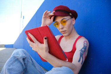 Sokakta rahatça otururken dijital tablet kullanan genç ikili olmayan kişi.