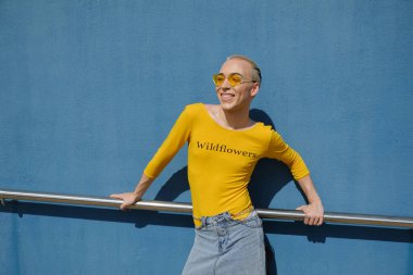 Güneş gözlüğü takan ve güneşli bir günde dışarıda poz verirken gülümseyen ikiyüzlü olmayan genç kişi..