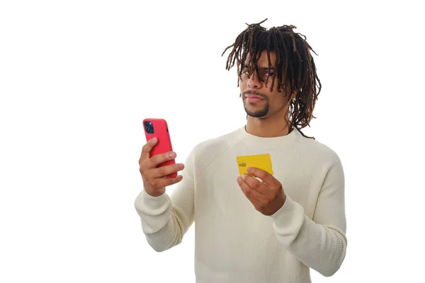 Hombre latino sosteniendo un teléfono móvil y una tarjeta de crédito mientras está parado sobre un fondo aislado. —  Fotos de Stock