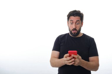 İzole edilmiş bir arka planda duran adam cep telefonuna şaşırmış görünüyor..