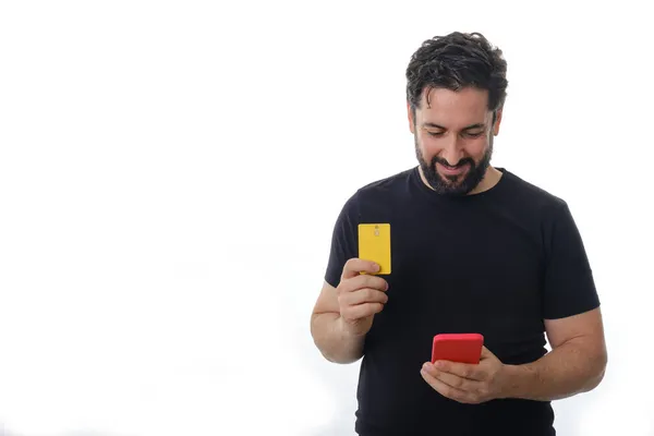 Hombre sosteniendo una tarjeta de crédito y usando un teléfono móvil mientras está parado sobre un fondo aislado. —  Fotos de Stock