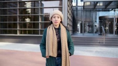 Asyalı Kadın ofis binasının önünde poz verirken kameraya bakıyor.