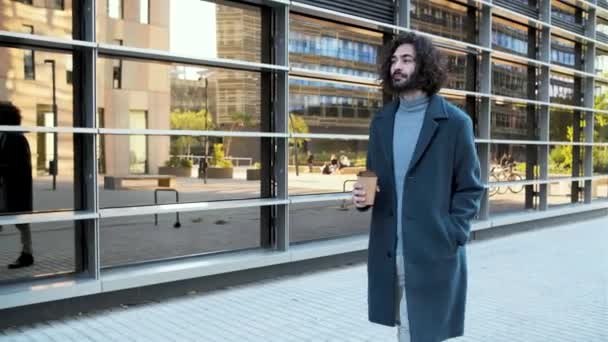 Молодой хипстерский бизнесмен улыбается и гуляет с кофе в деловом районе — стоковое видео