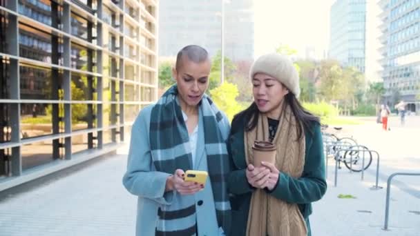 Aziatische en Kaukasische zakenvrouw met behulp van smartphone en het drinken van koffie in het financiële district — Stockvideo