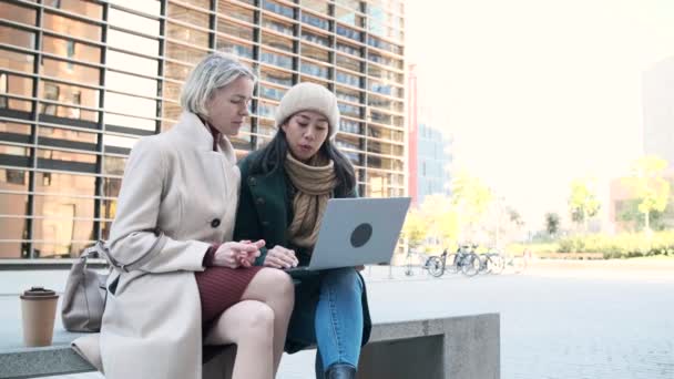 Азиатские и кавказские предпринимательницы, работающие на открытом воздухе и используя ноутбук — стоковое видео