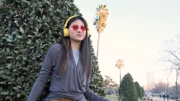 Asijské žena na sobě bezdrátové sluchátka těší poslech hudby a tanec venku ve městě ulici. — Stock video
