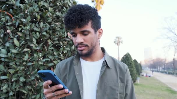 Afro-Mann lächelt, während er auf der Straße etwas liest oder auf seinem Handy sieht. — Stockvideo
