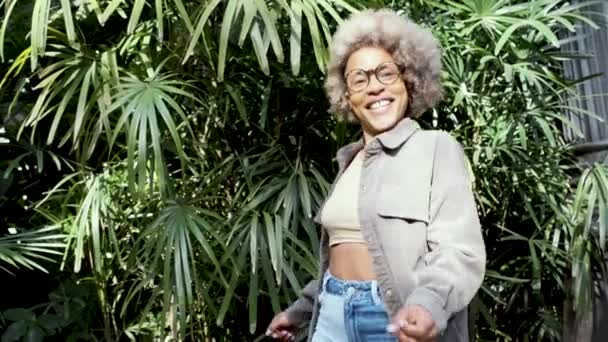 Fröhliche und aufgeregte Afro-Frau blickt in die Kamera, während sie auf einem natürlichen Hintergrund tanzt. — Stockvideo