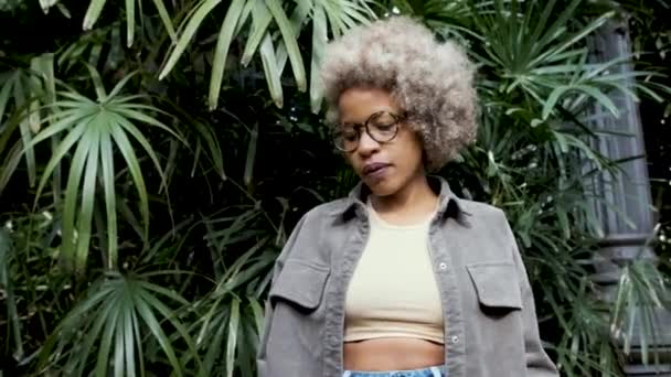 Afro mulher olha para a câmera enquanto começa a dançar com energia e alegria em um fundo natural. — Vídeo de Stock