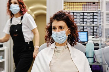 Kuaförde sandalyede otururken maske takan bir kadın..